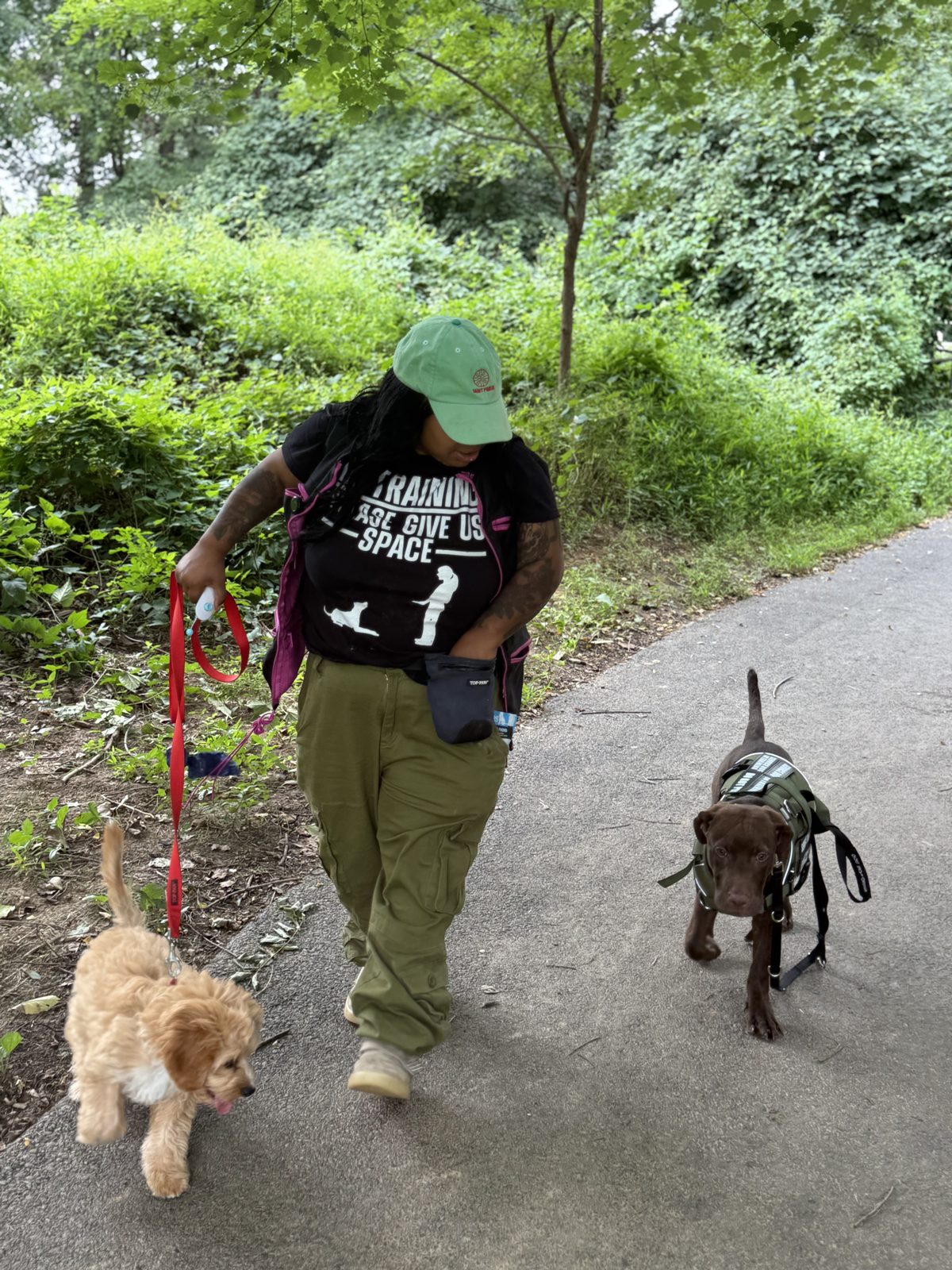 Jen walking a service dog in training and a puppy on a trail