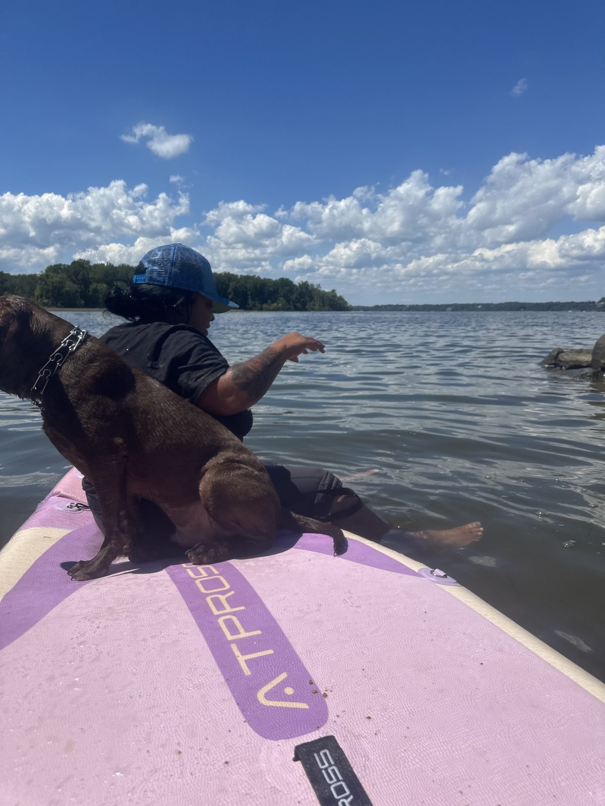 Jen and a dog relaxing together on a paddleboard on the lake